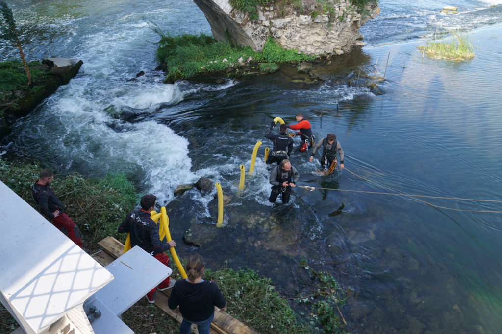 Installation de barres de blocage dans le Doubs à Dole, opérateurs harnachés travaillant en courant fort en amont du pont roman
